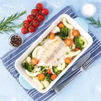 merluzzo di pesce al forno blu con verdure - broccoli, pomodori. cibo dietetico sano. sfondo di pietra blu, vista dall'alto.