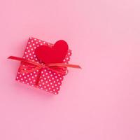 regalo in confezione regalo rossa con fiocco, cuore rosso, sfondo rosa, vista dall'alto, spazio vuoto per il testo. foto