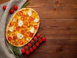 appetitosa focaccia dorata con pomodori, carne di pollo, spezie su tavola rustica di legno scuro foto