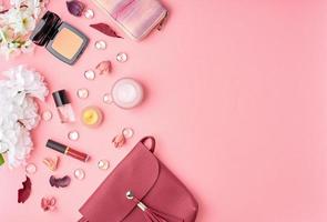 accessori donna piatti con cosmetici, crema viso, borsa, fiori su tavolo rosa brillante. foto