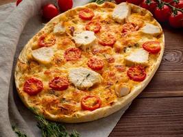 appetitosa focaccia dorata con pomodori, carne di pollo, spezie su tavola rustica di legno scuro foto