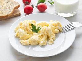 piatto bianco con uova strapazzate in padella su sfondo bianco chiaro con pomodori. foto