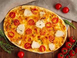 appetitosa focaccia dorata con pomodori, carne di pollo, spezie su tavola rustica di legno scuro foto