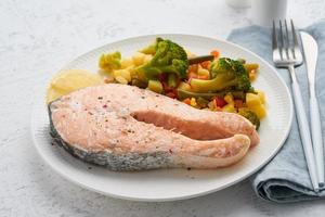 salmone e verdure al vapore, dieta sana. piatto bianco sul tavolo di cemento, vista laterale foto