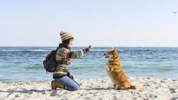 la giovane femmina felice cammina con il simpatico cane corgi sulla spiaggia soleggiata autunnale foto