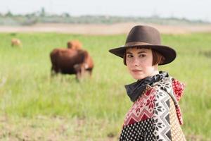 giovane viaggiatrice in poncho e cappello cammina nei campi e nella fattoria foto