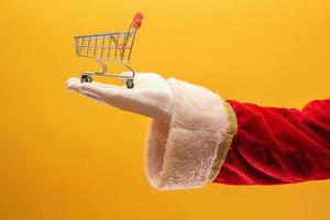 babbo natale e il supermercato, sta mostrando un mini carrello. concetto di natale e shopping. foto