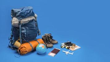 il concetto di organizzazione dell'attrezzatura per il viaggio messo sui bagagli. accessorio di concetto per le vacanze dei viaggiatori con una mappa, passaporto su sfondo di colore blu. zaino da viaggio foto