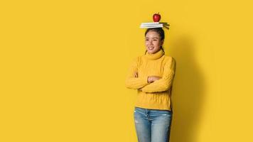 giovane donna allegra su sfondo giallo in studio con un libro e una mela rossa in testa. una ragazza sorridente e felice. il concetto di esercizio per una buona salute. amante della salute foto