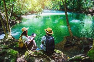 i viaggiatori si accoppiano con gli zaini seduti e si rilassano sugli scogli. viaggiare nella natura nella giungla verde e godersi la vista nella cascata. turismo, escursionismo, studio della natura. coppie che viaggiano per scattare foto