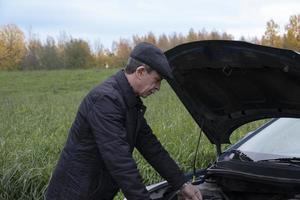 anziano pensionato apre il cofano della sua auto e guarda nel motore foto