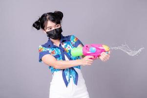 le belle donne asiatiche indossano una maschera chirurgica mentre tengono una pistola ad acqua di plastica durante il festival di Songkran foto