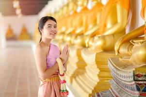 attraente donna tailandese in un antico abito tailandese tiene una ghirlanda di fiori freschi rendendo omaggio al buddha per esprimere un desiderio sul tradizionale festival songkran in tailandia foto