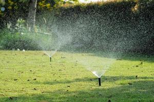 messa a fuoco selettiva sull'irrigazione a pioggia intorno al campo in erba con sfondo sfocato del giardino all'aperto foto