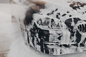 auto nera in schiuma di neve bianca durante il lavaggio e la pulizia dell'auto all'aperto foto