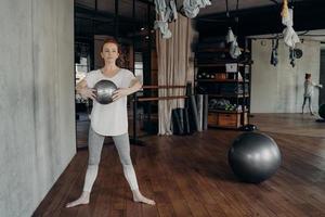 donna atletica concentrata in piedi nella posizione dei secondi piedi con fitball di dimensioni mini a braccia tese foto