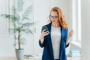 colpo alla vita di una donna d'affari di successo usa l'applicazione sul cellulare, legge le e-mail ricevute dal capo o dal collega, vestita con abiti formali, posa sopra l'interno dell'ufficio, scopre notizie finanziarie foto