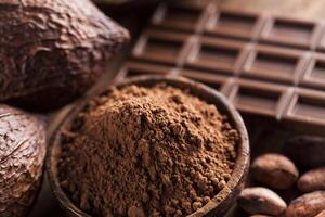 barretta di cioccolato, caramelle dolci, fave di cacao e polvere su fondo di legno foto