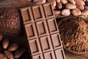 barretta di cioccolato, caramelle dolci, fave di cacao e polvere su fondo di legno foto