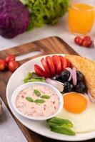 la colazione è composta da pane, uovo fritto, condimento per insalata, uva nera, pomodori. foto