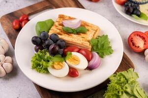 la colazione consiste in pane, uova sode, condimento per insalata di uva nera, pomodori. foto