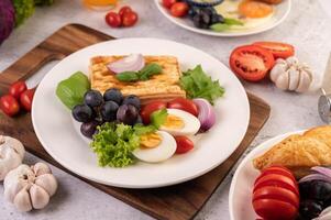 la colazione consiste in pane, uova sode, condimento per insalata di uva nera, pomodori. foto