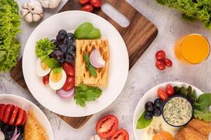 la colazione consiste in pane, uova sode, condimento per insalata di uva nera, pomodori. foto