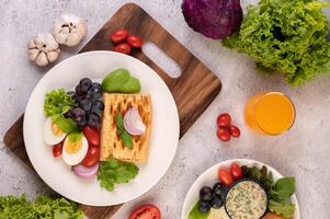 la colazione consiste in pane, uova sode, condimento per insalata di uva nera, pomodori. foto