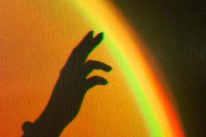 ombra della mano della donna. riflesso arcobaleno del raggio di sole sulla parete. la mano tocca l'arcobaleno.