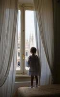adorabile bambina guardando fuori dalla finestra a duomo, milano, italia foto
