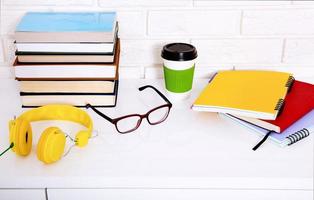 accessori per l'area di lavoro e l'istruzione sul tavolo. tazza di caffè, libri, occhiali, quaderni, cuffie. educazione allo stelo foto