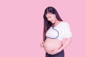 le donne asiatiche in gravidanza usano uno stetoscopio per toccarsi la pancia per ascoltare il loro bambino non ancora nato