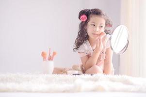 una simpatica ragazzina asiatica sta applicando felicemente i pennelli per il trucco con la cipria nella sua camera da letto foto
