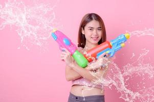 una bella donna asiatica mostra un gesto mentre tiene in mano una pistola ad acqua di plastica durante il festival di Songkran foto