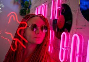 ragazza con luci al neon, bella donna con occhiali da sole, con i capelli rosa, con le trecce dreadlocks foto