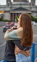 ragazza con una lunga e spessa oscurità che abbraccia un ragazzo dai capelli rossi con la maglietta blu sul ponte, amore per adolescenti foto