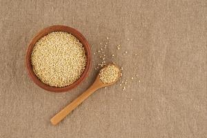 granella di semi di quinoa in ciotola di legno e cucchiaio su tovagliolo di lino, primo piano foto