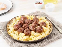 Polpette svedesi con pasta di fusilli su tavola di legno bianca, vista laterale foto