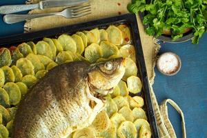 carpa al forno, pesce intero al forno con patate a fette su una grande teglia. piatto tradizionale polacco foto