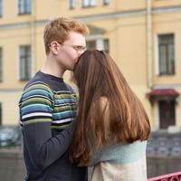 uomo dai capelli rossi bacia una donna in cima alla sua testa, un ragazzo con un maglione lenisce e conforta una ragazza con lunghi capelli scuri e folti foto