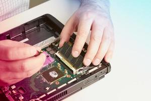 l'uomo ripara il computer. un tecnico dell'assistenza in camicia ripara il laptop, alla scrivania bianca contro il muro bianco. foto