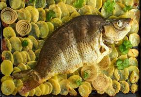 carpa al forno, pesce intero al forno con patate a fette su una grande teglia. piatto tradizionale polacco foto