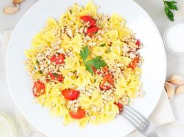 Farfalle con pomodori, carne di pollo, prezzemolo su fondo di pietra bianca, dieta ipocalorica, vista dall'alto foto