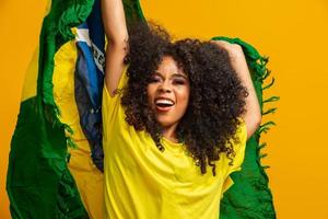 ragazza afro che fa il tifo per la squadra brasiliana preferita, con in mano la bandiera nazionale su sfondo giallo. foto