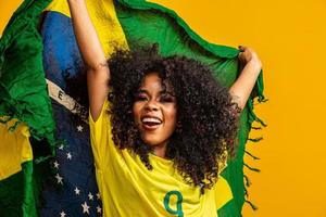 ragazza afro che fa il tifo per la squadra brasiliana preferita, con in mano la bandiera nazionale su sfondo giallo. foto