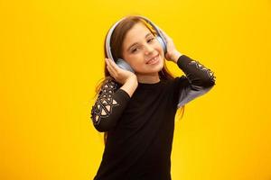 una piccola ragazza carina che si diverte ad ascoltare musica in cuffia isolata su sfondo giallo. foto