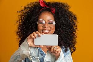 ritratto frontale di giovane donna afroamericana sorridente che guarda il cellulare con gli occhiali. bella ragazza con i capelli ricci che usa il suo smartphone per chattare con gli amici. concetto connesso foto