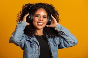 concetto di persone, musica, emozioni. felice donna spensierata con acconciatura afro balla al ritmo della melodia, chiude gli occhi ascolta una canzone ad alto volume in cuffia. bella donna afro con le sue cuffie foto