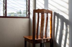 dietro lo schienale di una sedia di legno con le finestre a persiana sulla parete della stanza. foto