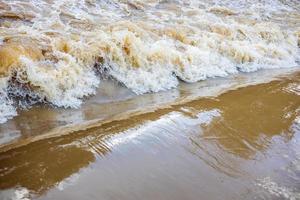 sfondo della superficie torbida dell'onda di marea marrone che inonda turbolentamente gli sbarramenti di straripamento. foto